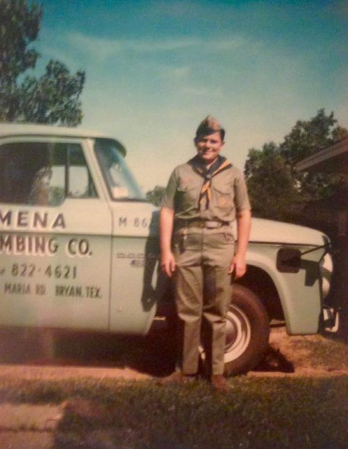Image of young Randy Mena in his boy scout uniform in front of vintage Mena Plumbing truck.